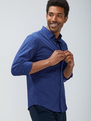 Men's indigo grey jaspe grid aero button down and navy kinetic pant model facing sideways with sleeves rolled buttoning shirt