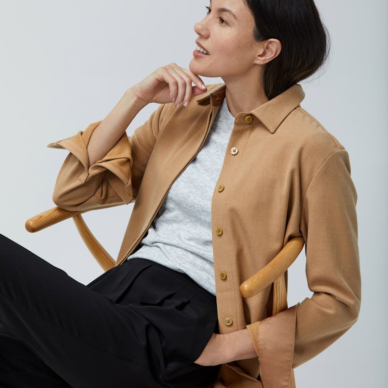 Women's Camel Fusion Overshirt layered over Light Grey Composite Merino Tee and Women's Black Swift Drape Pant on Model sitting in chair