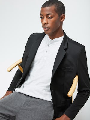 Men's Grey Heather Composite Merino Short Sleeve Henley under Men's Black Kinetic Blazer on model sitting in chair
