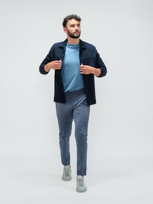 Man stretching his right leg and wearing kinetic jogger pants in indigo heather, a composite active tee in chambray blue, and a fusion chore coat in navy