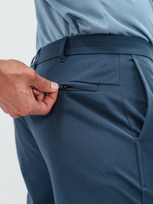 Close up shot of a man unzipping the back pocket on a pair of Pace tapered chino pants in faded indigo