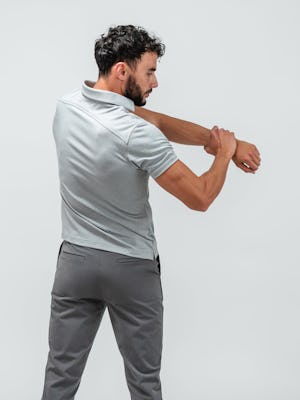 Man facing away from camera and stretching his left arm while wearing the apollo polo in pale grey heather
