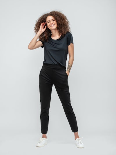 Woman with curly hair wearing black short sleeve luxe touch tee and black kinetic pull on pants with white sneakers