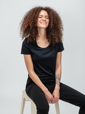 Woman with curly hair wearing black short sleeve luxe touch tee and sitting on a stool
