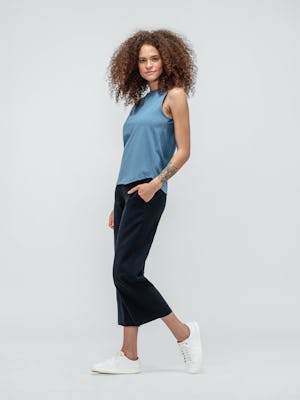 Woman with curly hair wearing blue composite merino tank top and navy swift drape pants with sneakers