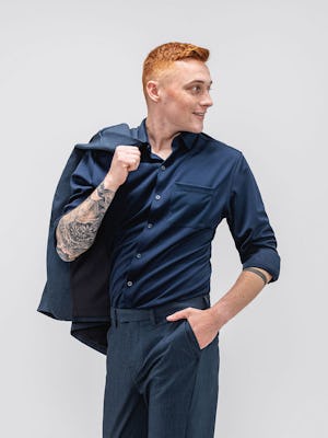 model wearing men's navy apollo sport shirt and azurite heather velocity pant facing forward with hand in pocket and velocity suit jacket slung over the shoulder