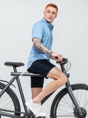 model wearing men's steel blue apollo short sleeve sport shirt and navy kinetic shorts on bicycle