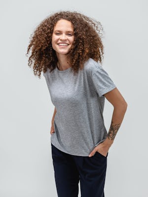 model wearing pale grey heather composite merino boxy tee and navy swift drape pant leaning forward with hands in pockets