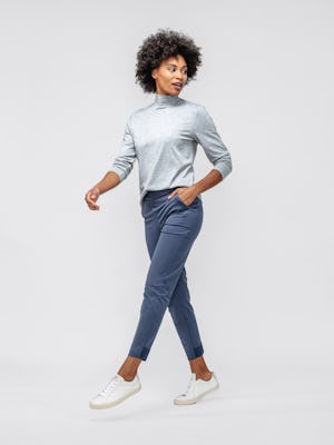model wearing women's pale grey heather composite merino mock neck and slate blue kinetic pull-on pant hopping forward with sleeves pulled up and hand in pocket