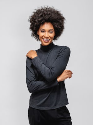 model wearing black composite merino mock neck and black swift drape pant facing forward with arms wrapped around her body