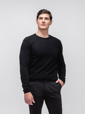 model wearing men's black kinetic tapered pant and black atlas merino crew neck sweater facing forward with hand in pocket