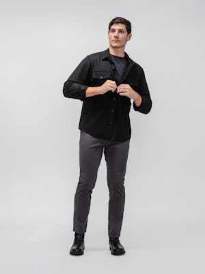 Model wearing Charcoal Kinetic Tapered Pant and Black Fusion Overshirt and Black Composite Merino Long Sleeve Tee facing forward and buttoning overshirt