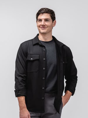 Model wearing Charcoal Kinetic Tapered Pant and Black Fusion Overshirt and Black Composite Merino Long Sleeve Tee facing forward with hand in pocket
