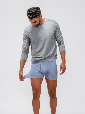 model wearing men's light blue heather composite merino boxer brief and grey composite merino long sleeve tee facing forward with sleeves pushed up and stretching boxer fabric