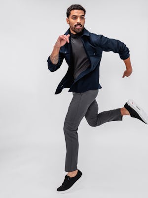 model wearing men's grey heather velocity flannel pant and navy fusion overshirt and dark charcoal composite merino mock neck sleeves rolled up and leaping in the air
