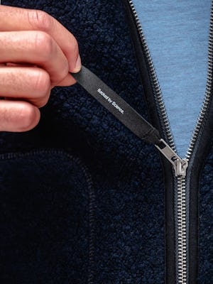 close up of model wearing navy composite merino ecofleece and stone blue composite merino active tee showing "backed by science" logo on zipper pull