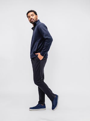 model wearing men's indigo heather hybrid 1/4 zip pullover and dark navy pace tapered chino facing to the side with hand in pants pocket