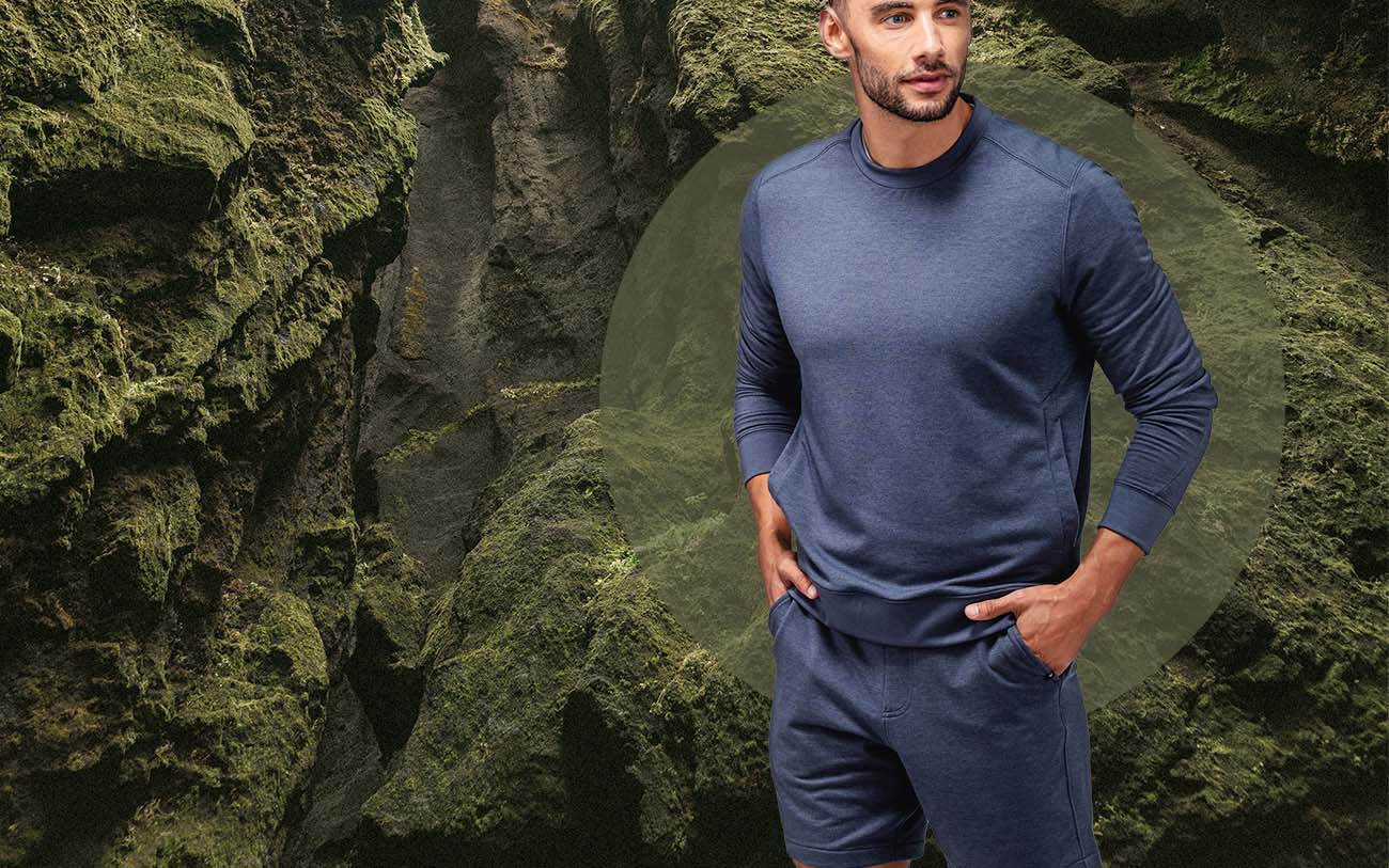 model wearing men's fusion terry sweatshirt standing in front of a mossy background