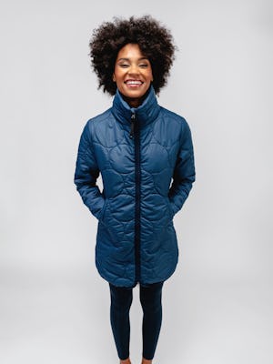 model wearing women's storm blue aurora insulated jacket and navy joule active legging facing forward with hands in pockets