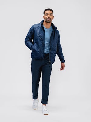 model wearing navy aurora jacket and kinetic twill 5-pocket pant and stone blue composite merino tee facing forward with hand in pocket