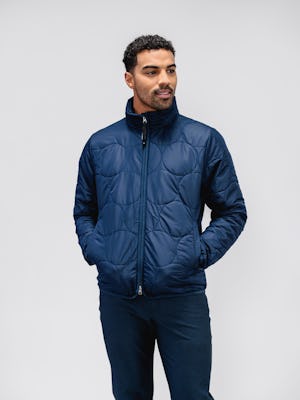 model wearing men's navy aurora jacket and steel blue heather kinetic twill 5-pocket pant facing forward with jacket zipped and hands in pockets