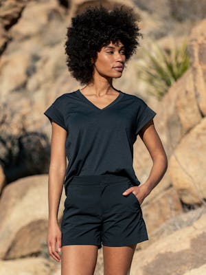 model wearing black composite merino v-neck tee and black pace poplin short facing forward with hand in pocket