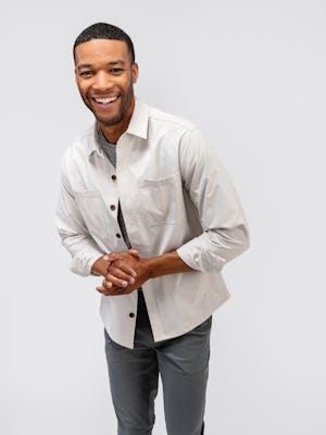 model wearing mens pace poplin overshirt stone and mens kinetic tapered pants slate greya and mens composite merino tee pale grey heather hands together standing up shot