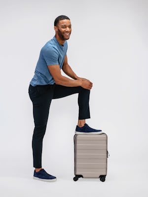 model wearing mens pace poplin chino navy and mens composite merino tee stone blue with leg on suitcase 