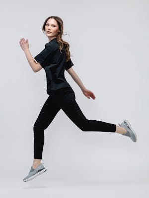 model wearing women kinetic pull on pant black and black juno boxy blouse running looking at camera both legs in air