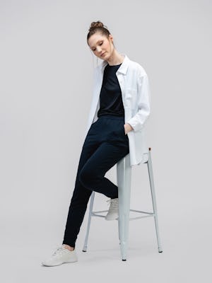model wearing white aero zero oversized shirt and black luxe touch tee and black fusion terry jogger sitting on stool with shirt unbuttoned and hands in pockets