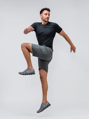 model wearing mens kinetic pull on short slate grey and men composite merino active tee black jumping one leg in air