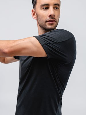 model wearing black composite merino active tee facing forward and doing an arm stretch