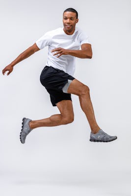 model wearing mens apollo x active tee white and mens newton active short black jumping both legs in air