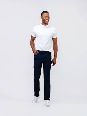 model wearing mens kinetic twill 5 pocket pant navy heather and mens high crew atlas tee white full body front one hand in pocket