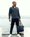 model wearing mens fusion double knit quarter zip charcoal heather carrying duffle bag looking sideways on ship deck