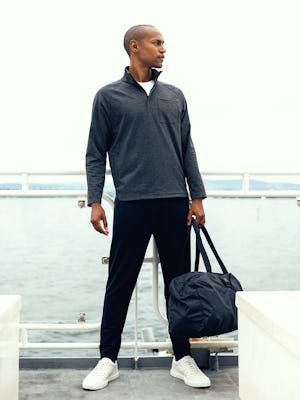 model wearing mens fusion double knit quarter zip charcoal heather carrying duffle bag looking sideways on ship deck