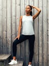 model wearing womens composite merino active tank pale grey heather and womens joule active legging black one hand on head standing on steps lifestyle 1x1
