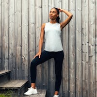 model wearing womens composite merino active tank pale grey heather and womens joule active legging black one hand on head standing on steps lifestyle 1x1