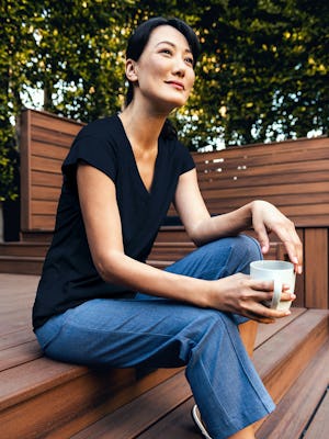 Woman wearing navy composite merino v-neck tee and calcite heather velocity pull-on pant sitting on steps with coffee in hand