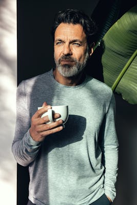 Men's Composite Merino Long Sleeve Tee in Pale Grey Heather on model standing in front of plant holding coffee cup
