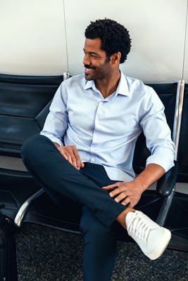 Men's Chambray Blue Aero Zero Dress Shirt on model sitting in airport with crossed legs