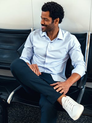 Men's Chambray Blue Aero Zero Dress Shirt on model sitting in airport with crossed legs