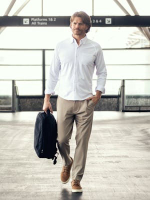 model wearing mens velocity pull on pant flax carrying aer backpack one hand in pocket lifestyle