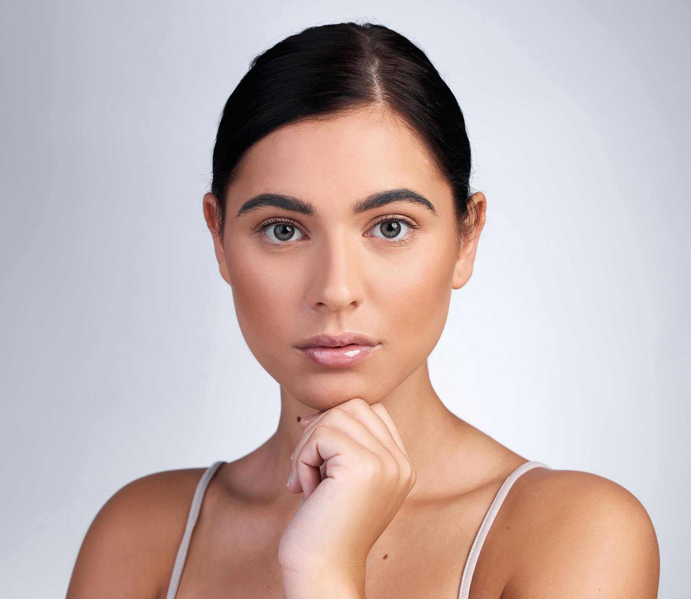 woman in white camisole touches her chin with dark hair in a bun