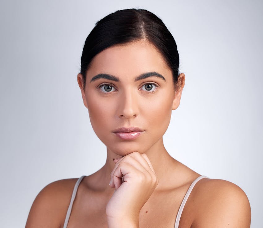woman in white camisole touches her chin with dark hair in a bun