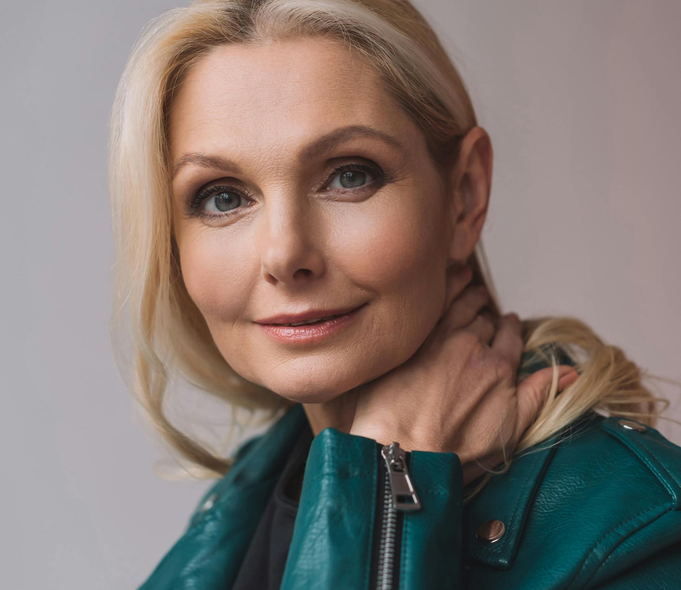 woman in turquoise leather jacket holder her neck