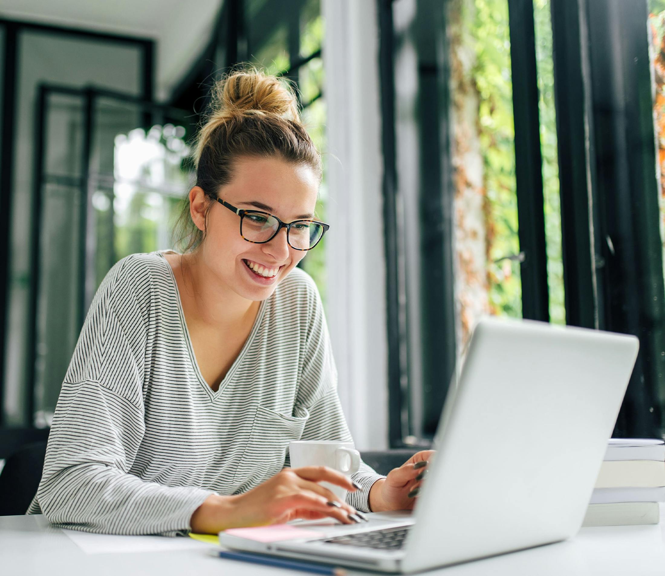 blonde woman with hair in bun wearing glasses looking at her laptop