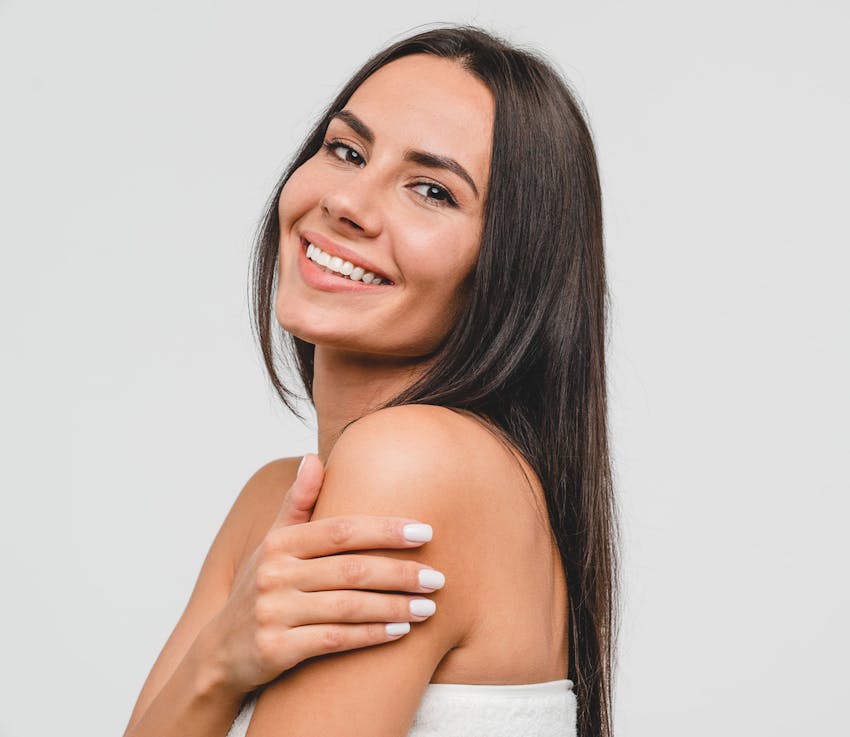 woman with straight brown hair smiling with her hand on her arm