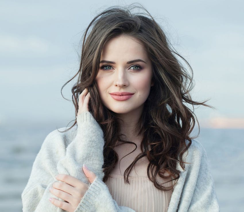 woman in grey sweater and cream shirt touching her jaw