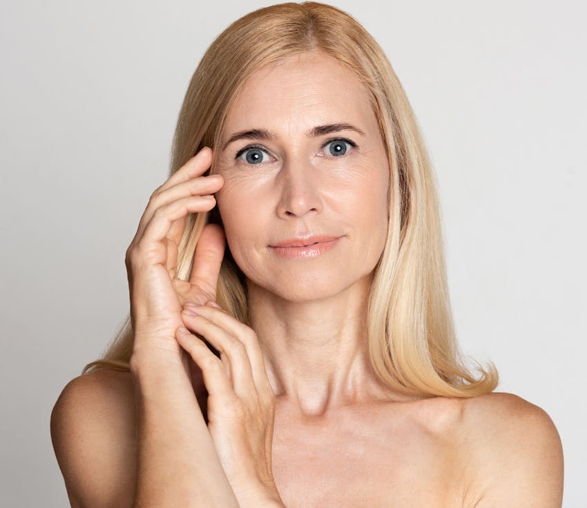 woman with blond hair touches temple looking forward